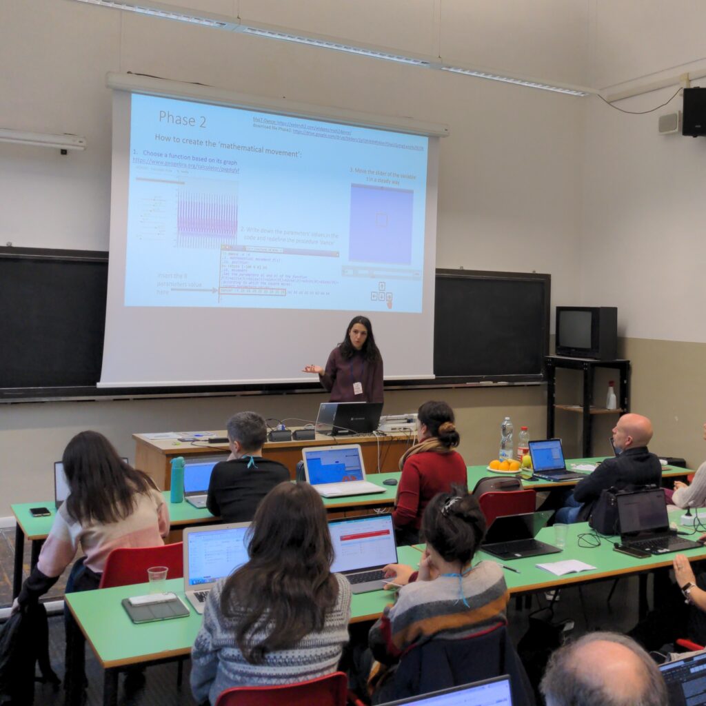 A classroom with a speaker presenting on a projector and participants sitting with laptops.