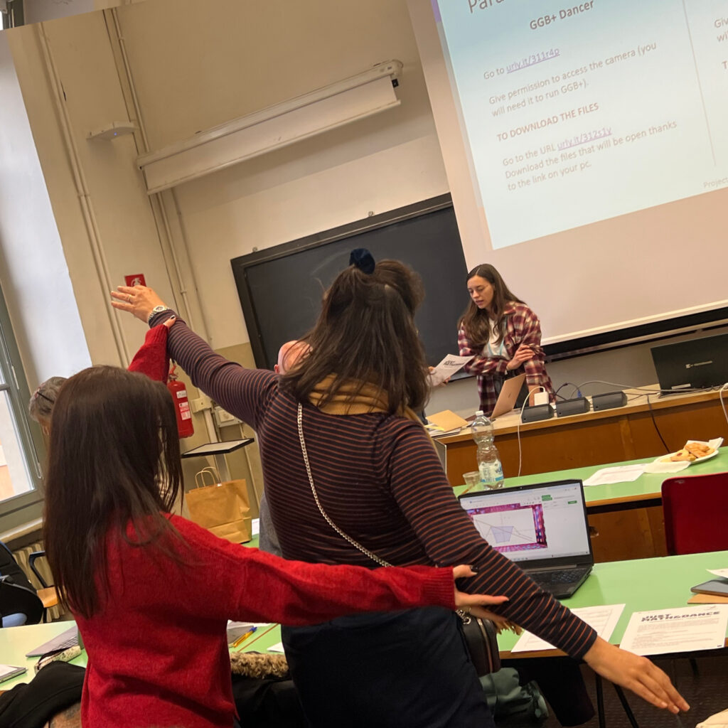 One workshop participant helping another participant perform a pose of aligning their outstretched arms at a certain angle in front of a laptop.