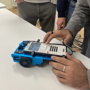 A person typing commands on a small console connected to a robot with wheels.