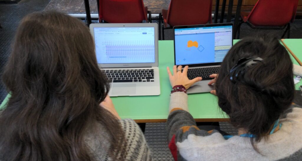 Two workshop participants working on two laptops. One laptop shows the Malt Dance application with motion tracking. The other computer shows a GeoGebra applet where the participant can define a function through multiple parameter sliders.