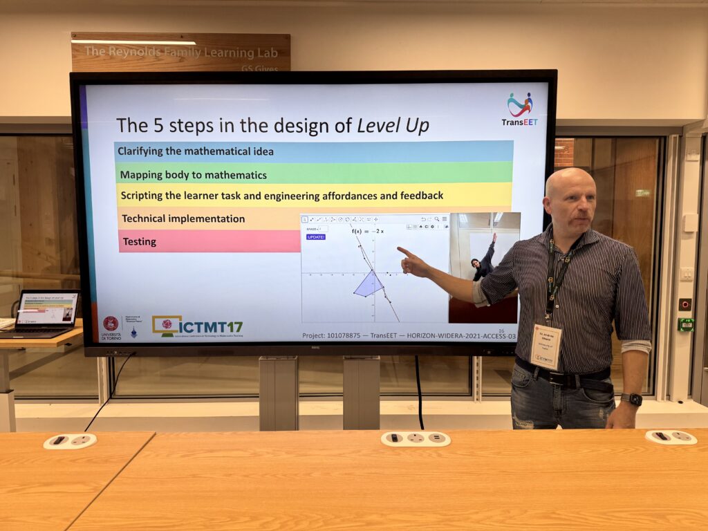 Andrea Ghersi points to a presentation slide titled “The 5 steps in the design of Level Up” during ICTMT 17 in London. The slide lists five design steps for a GeoGebra Plus applet, such as Clarifying the mathematical idea, Mapping body to mathematics, Scripting the learner task and engineering affordances and feedback, Technical implementation, Testing and shows a small image of a participant interacting with the app.