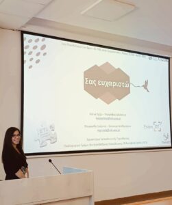 A photo of Katia Schiza presenting in a lecture room with a slideshow projected on the wall behind her.